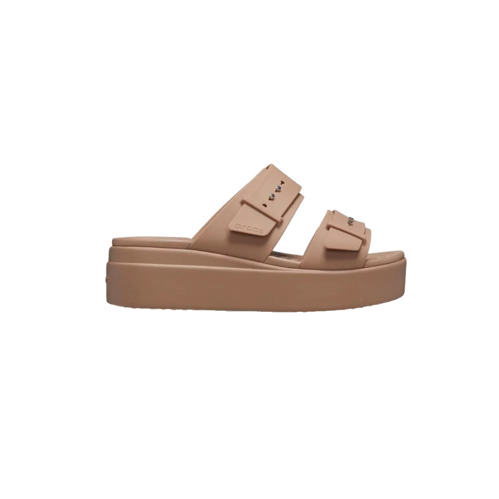 ה-Crocs Brooklyn Bucle Lowwdg 207431-2Q9 מבית Crocs הוא סנדל פלטפורמה בצבע בז' עם שתי רצועות רחבות, עיטורי חתיכים מתכתיים וסוליה עבה, המוצג בפרופיל על רקע לבן חלק.