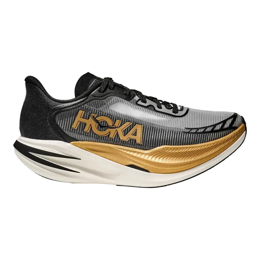 ה-Hoka 1162053/BKGD U CIELO X1 2.0 BLACK/GOLD הוא נעל ריצה בצבעים שחור, אפור וזהב עם סוליה לבנה עבה, שרוכים שחורים ולוגו Hoka בולט בצד.