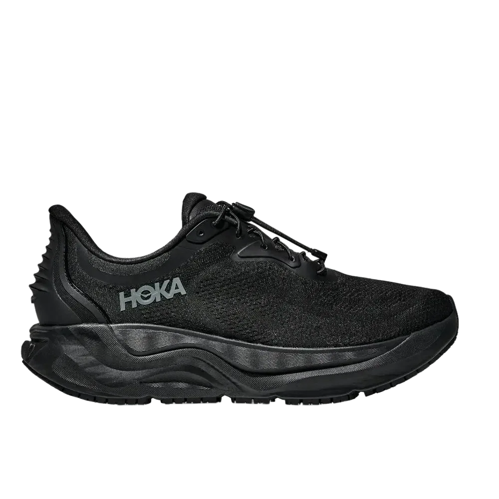 Hoka ARAHI SR WIDE (2E) 1168714/BBLC BLACK הוא נעל ריצה שחורה עם חלק עליון מרשת, סוליה מרופדת ולוגו HOKA בצד, המוצגת בפרופיל צדדי על רקע לבן חלק.