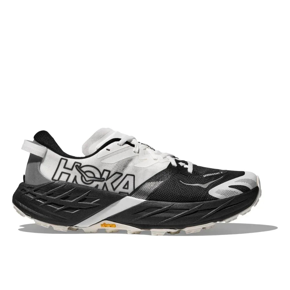 Hoka 1171930/BWHT SPEEDGOAT 7 WIDE BLACK/WHITE הוא נעל ריצה בשחור-לבן עם סוליה מרופדת, לוגו "HOKA" בולט בצד ושרוכים לבנים.