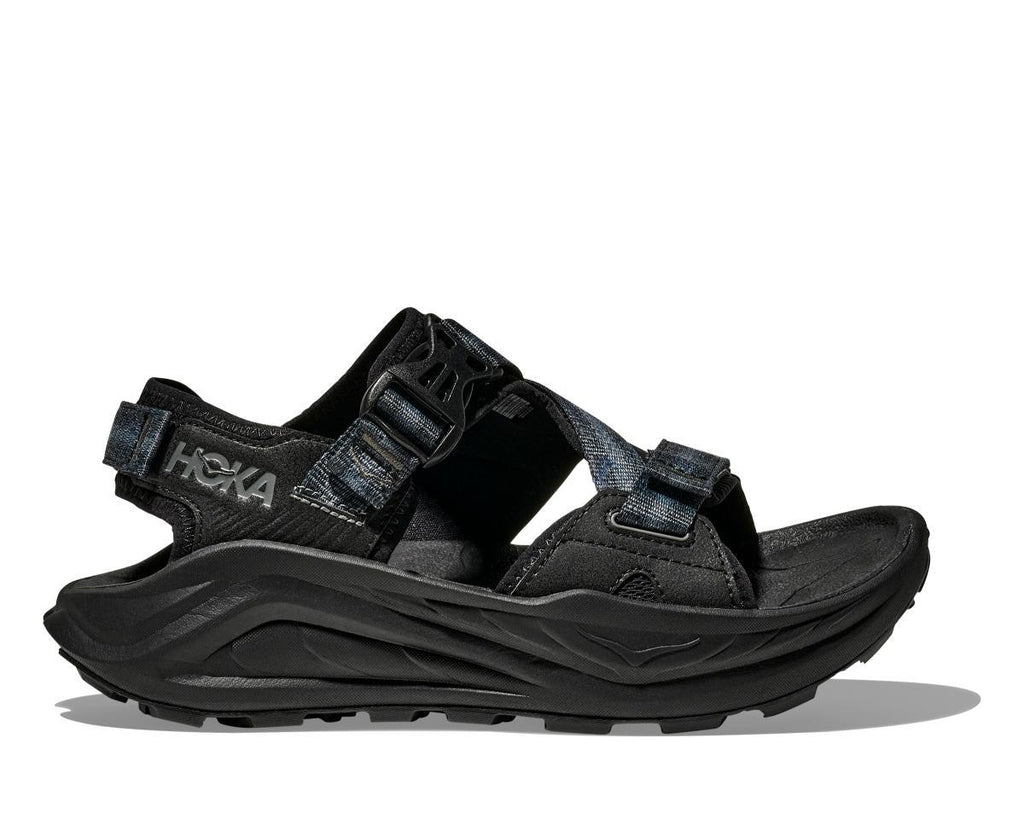ה-Hoka INFINI HIKE TC 1162570/BBLC BLACK הוא סנדל שחור לטיולים עם רצועות מתכווננות, סוליה מרופדת ודפוס סוליה בולט, המוצג על רקע לבן חלק.