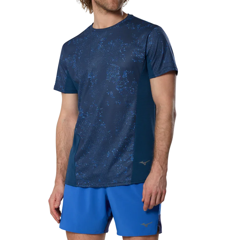 גבר לובש את חולצת הטי עם שרוולים קצרים Mizuno Graphic (מידה M) בצבע כחול אסטט (J2GAD00412) מבית Mizuno, עומד בביטחון על רקע לבן חלק.