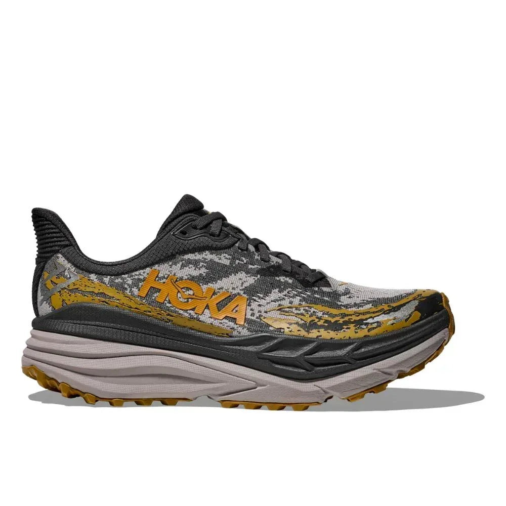 ה-Hoka STINSON 7 BLACK/CEMENT (1141530/BCMN) היא נעל ריצה בצבעים אפור ושחור עם נגיעות צהובות, סוליה מרופדת ועבה, אשר תוכננה כדי להבטיח נוחות וביצועים. מוצגת על רקע לבן חלק.