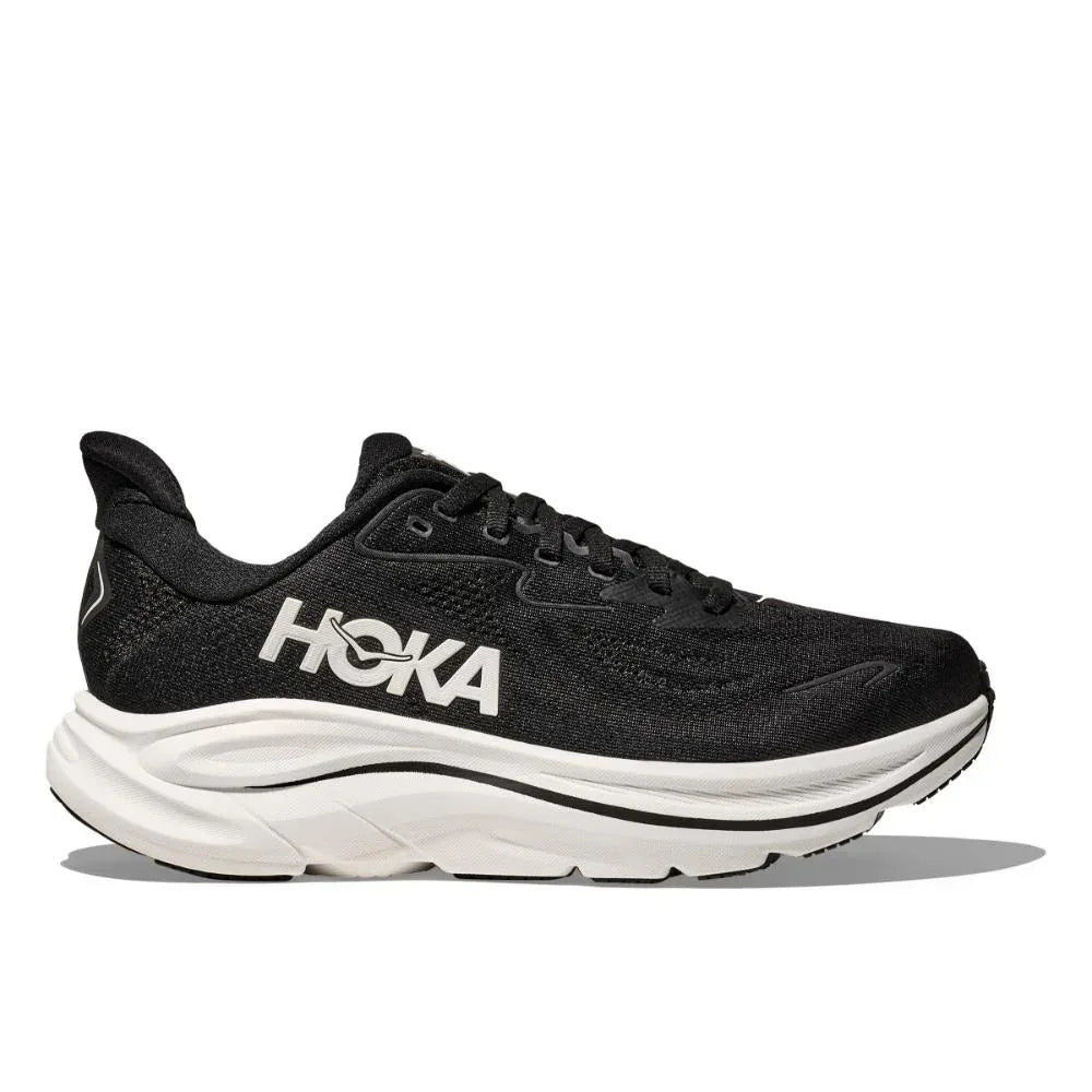 ה-Hoka CLIFTON 10 X-WIDE 1162052/BWHT היא נעל ריצה שחורה עם סוליה לבנה ולוגו Hoka לבן בצד, המוצג בפרופיל צדדי על רקע אחיד.