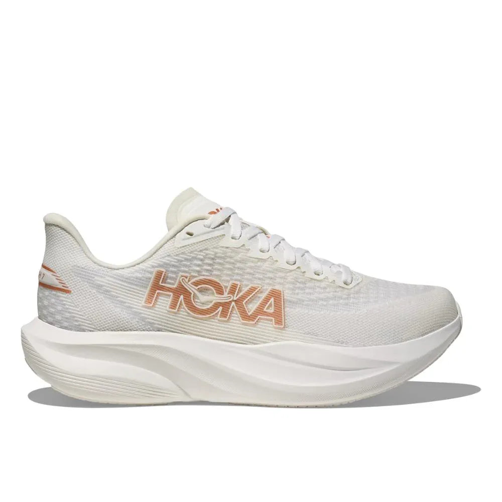 ה-Hoka MACH 7 WIDE (D) 1171906/FTRS FROST/ROSE GOLD היא נעל ריצה ספורטיבית בצבע לבן עם סוליה מרופדת ועבה, ועליה לוגו "HOKA" בצבע חום בהיר בצד, כפי שנראה בתמונה משמאל.