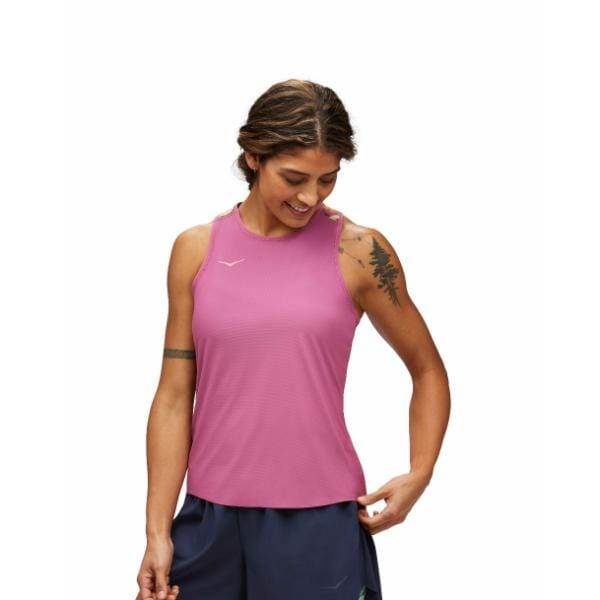 אדם שלובש Hoka 1151082/BET AIROLITE RUN TANK ומכנסיים קצרים כחול כהה מביט למטה ולשמאלו. יש להם קעקועים על זרועם הימנית והם עומדים על רקע לבן רגיל.