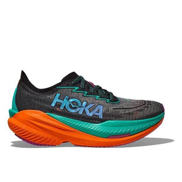 מבט מהצד של נעל הריצה Hoka 1162390/BCQ MACH X2 WIDE (2E), מציגה את ערכת הצבעים השחור, הירוק והכתום שלה. הנעל כוללת סוליה עבה ומרופדת עם שם המותג "HOKA" מוצג בולט בצד.