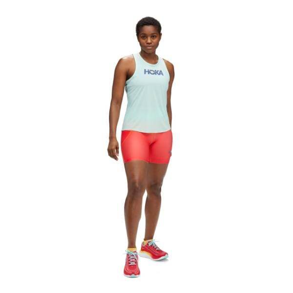 אדם שלובש Hoka 1151082/CTH Airolite Run Tank בתכלת, מכנסיים קצרים אדומים ונעלי ריצה אדומות עומד עם הפנים קדימה.