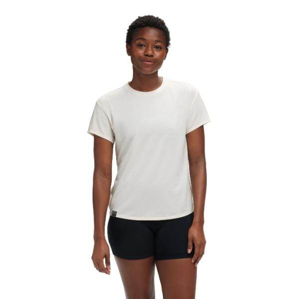 אדם לובש את Hoka Essential Tee ב- Eggnog בשילוב עם מכנסיים קצרים שחורים, עומד על רקע לבן.