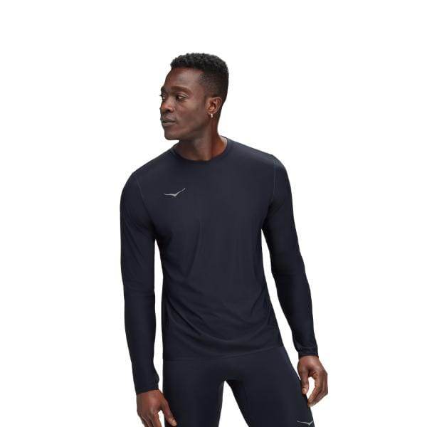 אדם שלובש Hoka 1151072/BLK M Airolite Run Long Sleeve ומכנסיים שחורים עומד על רקע לבן רגיל.