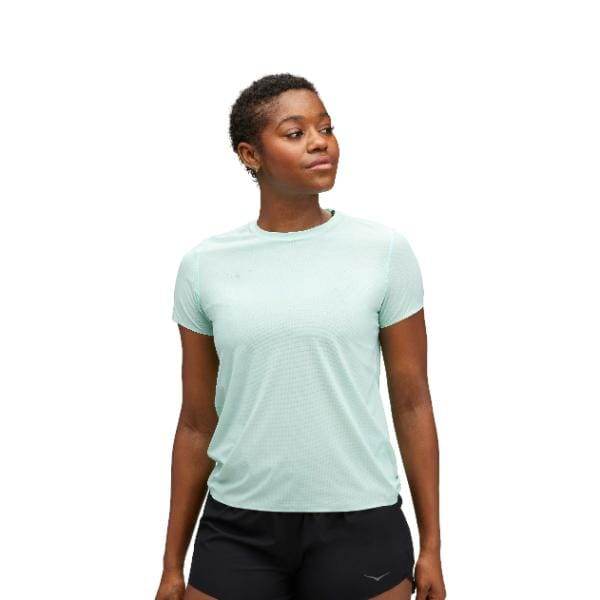 אדם לובש Hoka 1151084/CLDL AIROLITE RUN SHORT SLEVE במכנסיים קצרים בירוק בהיר ושחור, עומד עם הבעה ניטרלית על רקע רגיל.