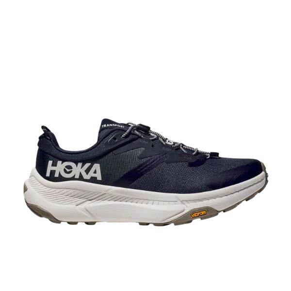 נעל אתלטית Hoka 1164370/VYN TRANSPORT WIDE (2E) בצבע כהה עם סוליה לבנה ומיתוג Hoka, מוצגת בפרופיל צד.