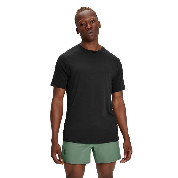גבר לובש חולצת טריקו שחורה של On Cloud 1ME11460553 Focus-T ומכנסיים קצרים ירוקים עומד על רקע לבן.