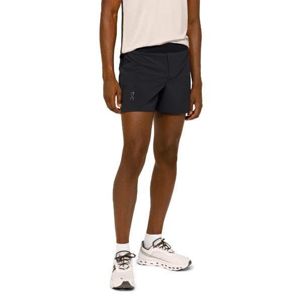 אדם בחולצה לבנה ללא שרוולים ובמכנסיים קצרים קלים בגודל 1ME11560553 On Cloud 1ME11560553, בשילוב עם נעלי ספורט לבנות, עומד במבט חלקי בפרופיל.