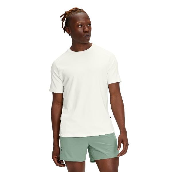 משפט עם מוצר הוחלף: גבר לבוש ב-On Cloud 1ME11460069 Focus-T חולצת טריקו לבנה ומכנסיים קצרים ירוקים עומד על רקע לבן.