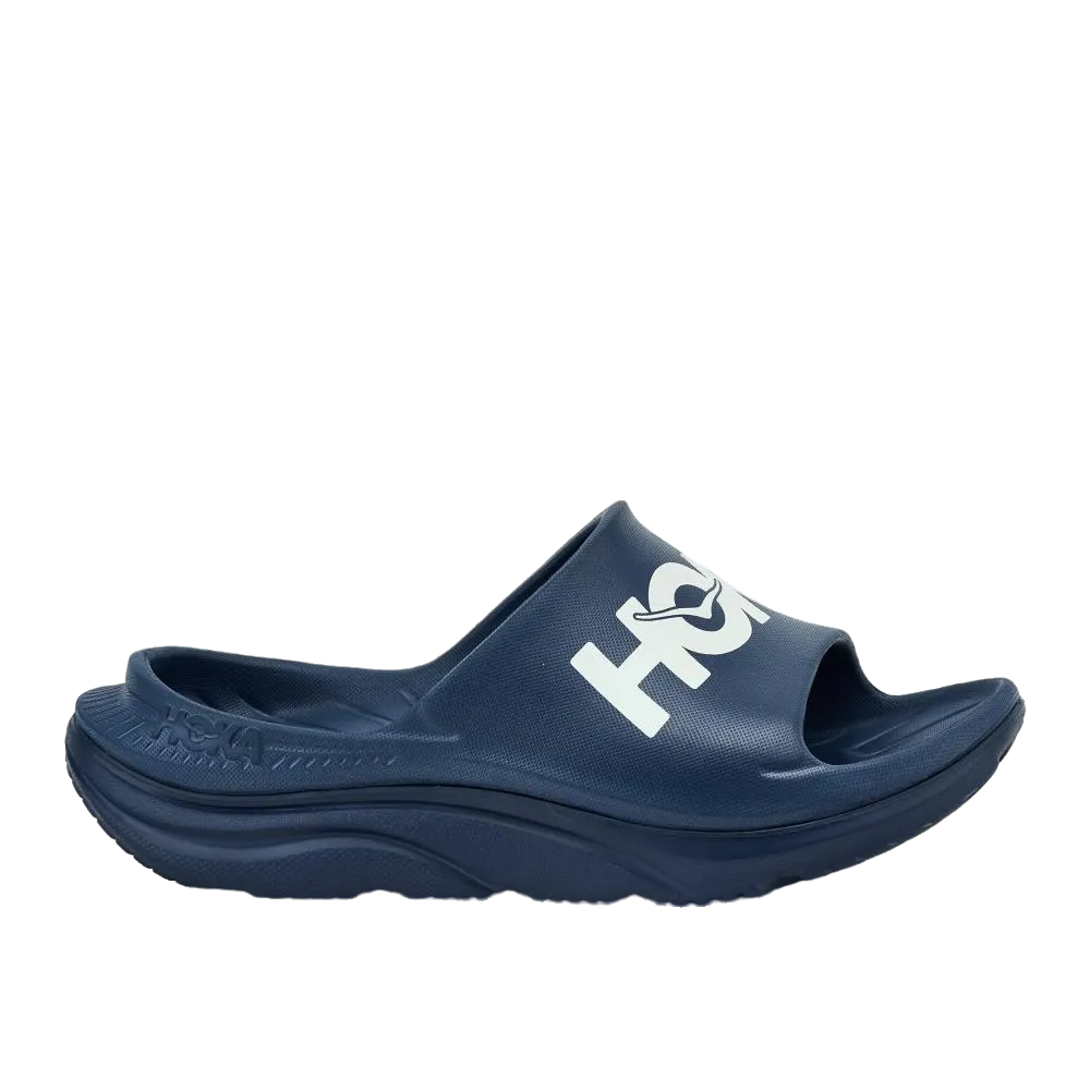 כפכפי הוקה "ORA ATHLETIC SLIDE" לגברים ולנשים, דגם U ORA ATHLETIC SLIDE 1155154/VYN Navy, הם כפכפים בצבע כחול כהה עם סוליה עבה והכיתוב "HOKA" בלבן — כפכפי התאוששות מושלמים לאחר אימונים.