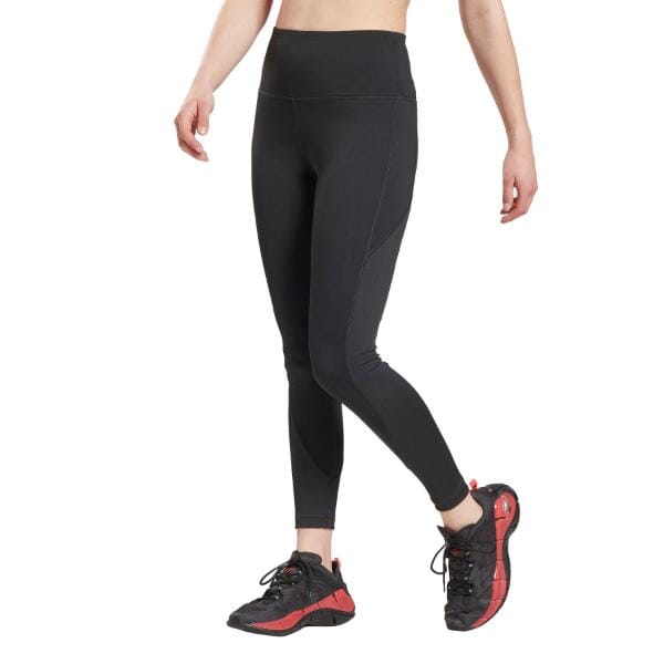 אישה לובשת חותלות שחורות של Reebok Wor Rib High Rise GR9507 ונעלי ספורט של ריבוק אדומות ושחורות, עומדת עם רגל אחת מורמת מעט, רקע לבן.