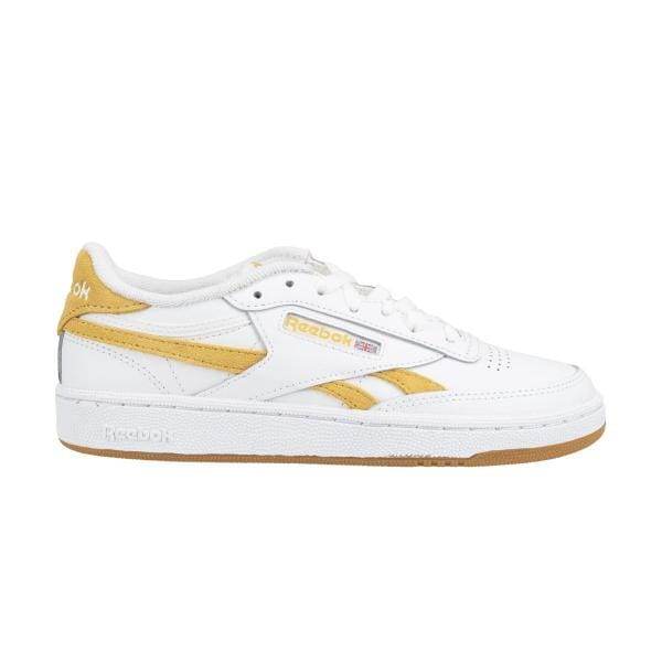 A Reebok Club C Revenge 100033437 עם הדגשים צהובים, הכולל את הלוגו של Reebok, שרוכים לבנים ומיתוג ריבוק צהוב על העקב והצד. לנעל סוליה לבנה עם סוליה חיצונית חומה בהירה.