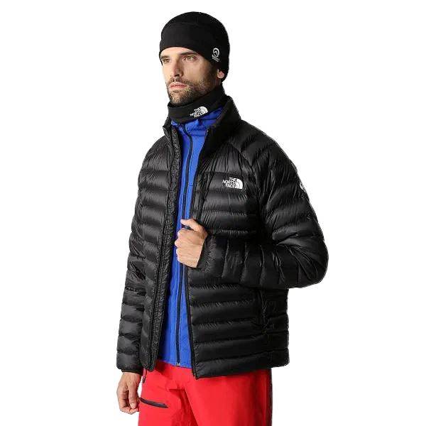 Man in The North Face Summit Breithorn ז'קט TA7UT9JK3, שכבה בינונית כחולה, מכנסיים אדומים, כיפה שחורה וקרסולית צוואר, עומדת על רקע שחור.