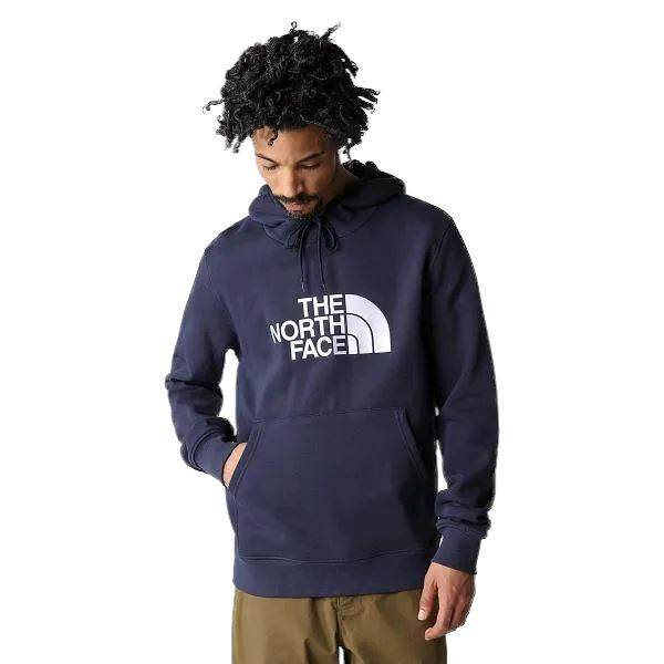 אדם עם שיער מתולתל לובש כחול כהה The North Face Drew Peak Pullover Hoodie T0AHJY8K2 ומכנסי חאקי מסתכל למטה עם יד אחת בכיס הקפוצ'ון.
