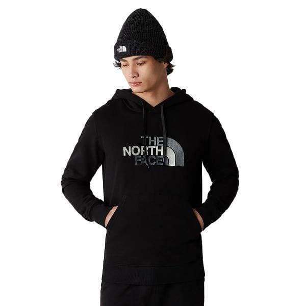 אדם שלובש קפוצ'ון מסוג The North Face Drew Peak Pullover T0AHJYKX7 וכופת סרוגה שחורה עם ידיו בכיס הקפוצ'ון ומסתכל למטה שמאלה.