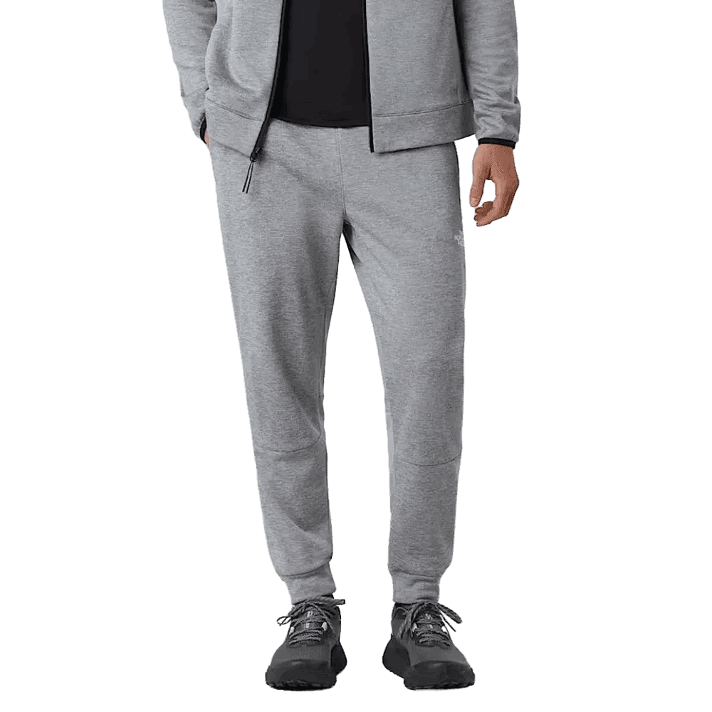 אדם לובש מכנסי פליס ארוכים גברים The North Face M MOUNTAIN ATHLETICS FLEECE PANT TA893SEB9 עם חולצה שחורה ונעלי ספורט, מוצג מהכתפיים ועד הרגליים על רקע אחיד.